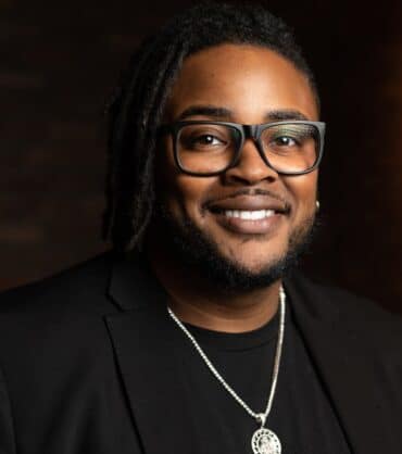 Marketing Co-founder Ken Floyd with glasses smiling in a dark background.